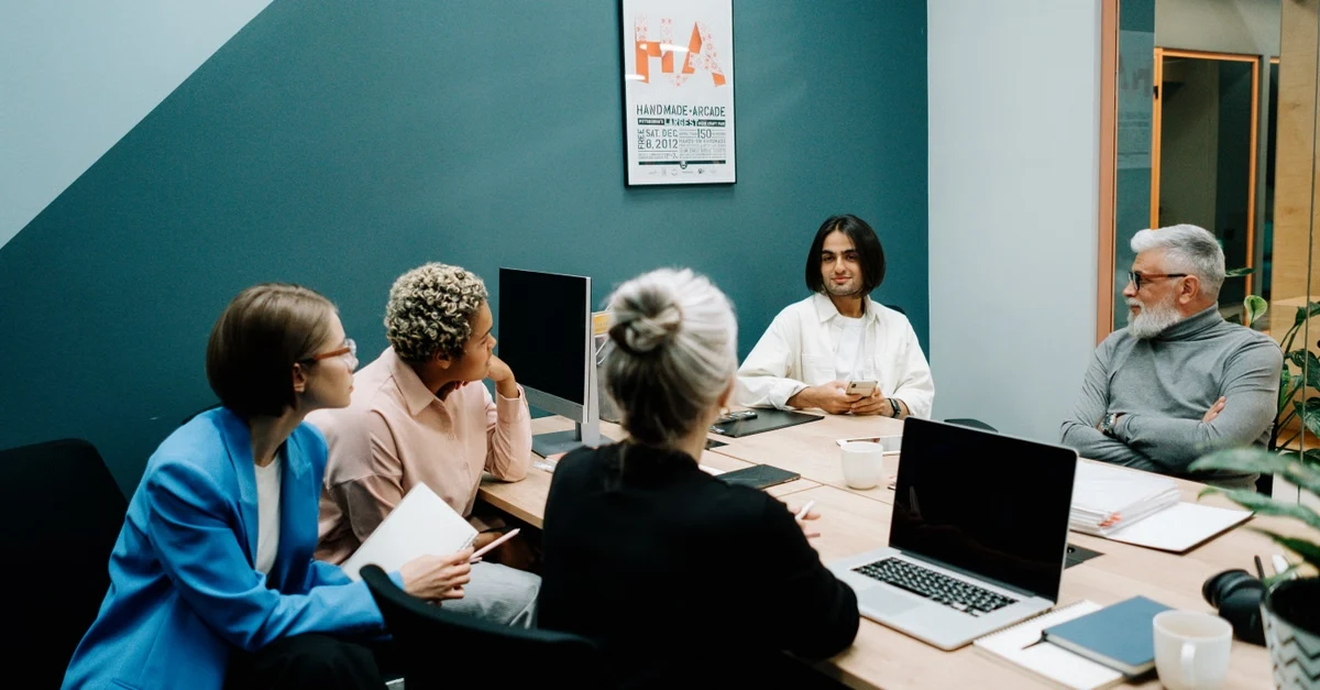 Project management executive assistants collaborating in modern teal conference room during team meeting.