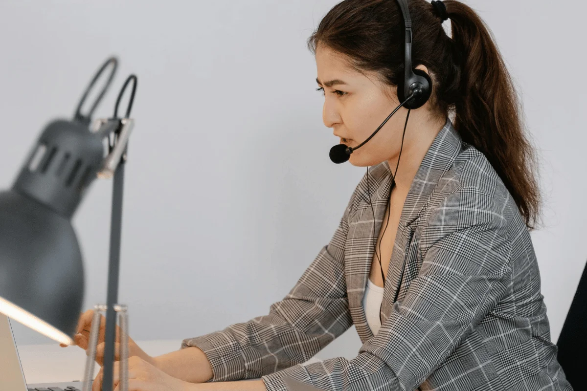 A focused female customer support representative wearing a headset and working on a laptop.