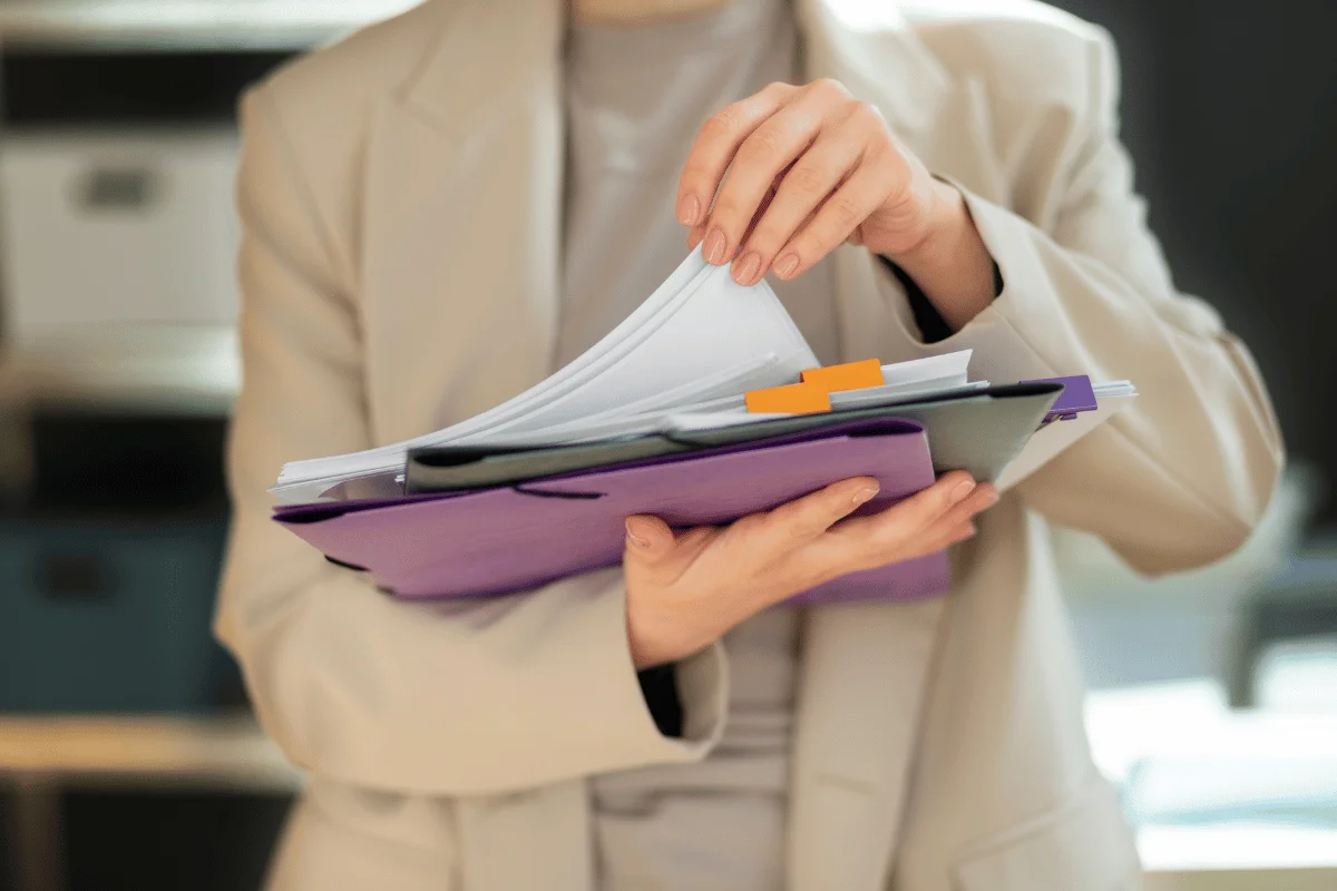 A person flipping through documents in a purple folder with tabs while holding it in one hand.