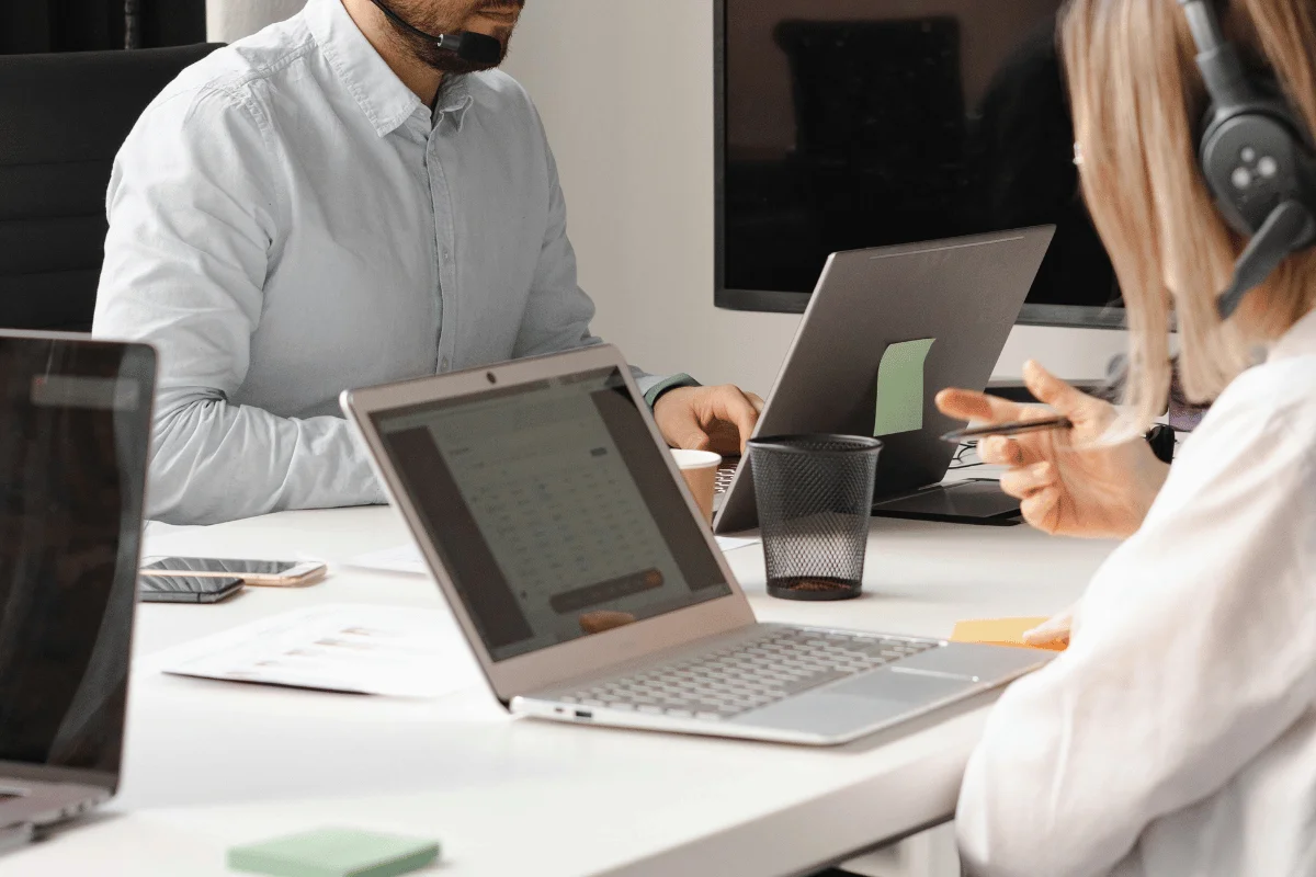 Team members working with laptops and headsets at a white desk.