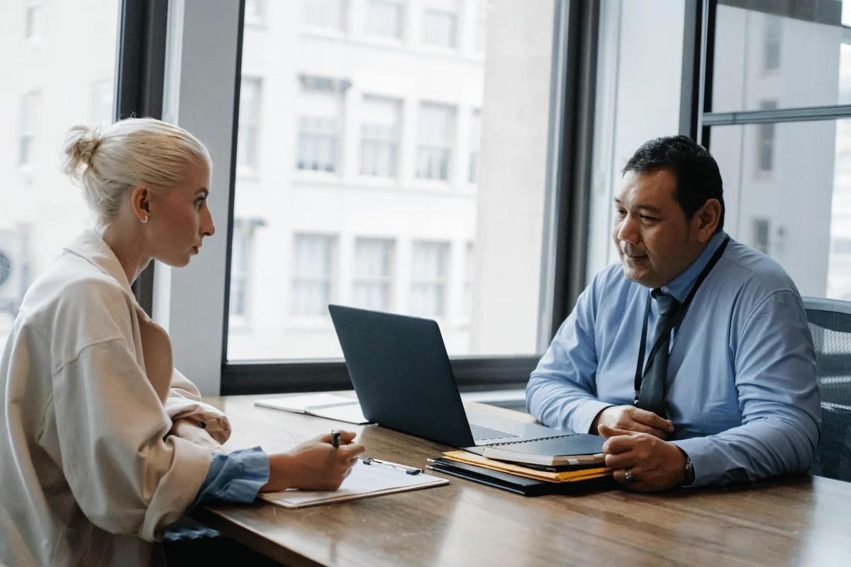 A businessman in a blue shirt discussing work with his assistant at a modern office desk.