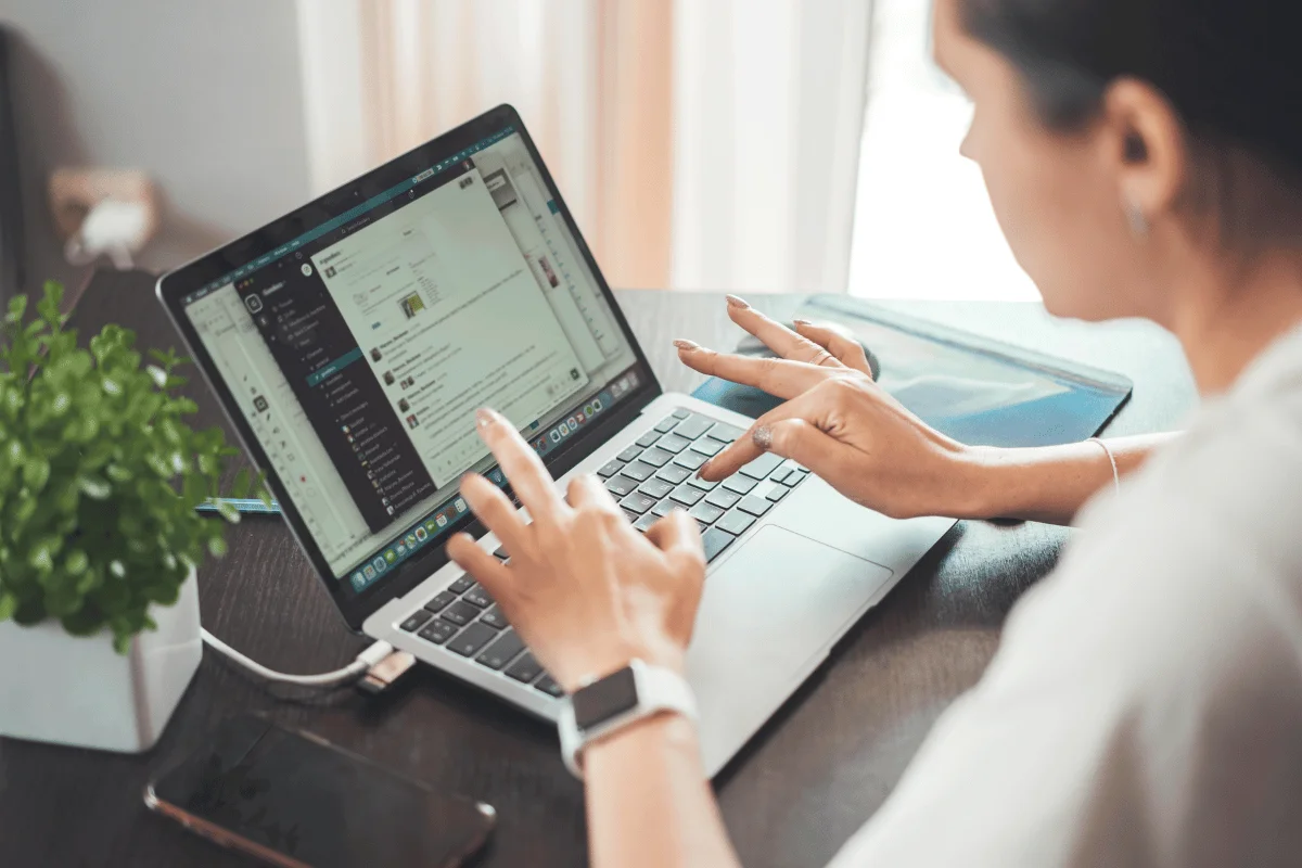 A professional woman working remotely, typing on a laptop while using a communication app.