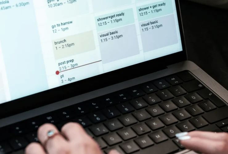 Hands typing on a laptop keyboard with a digital calendar showing schedule entries like brunch, shower, and Visual Basic classes.