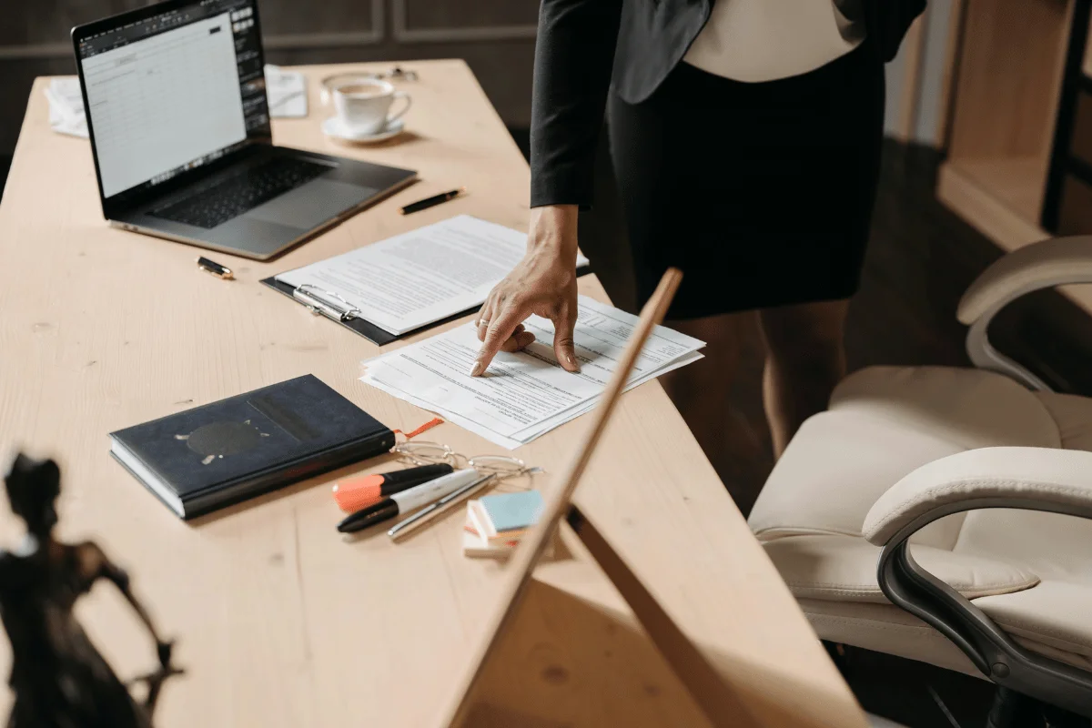 A professional woman in business attire pointing at legal documents on a wooden office desk.