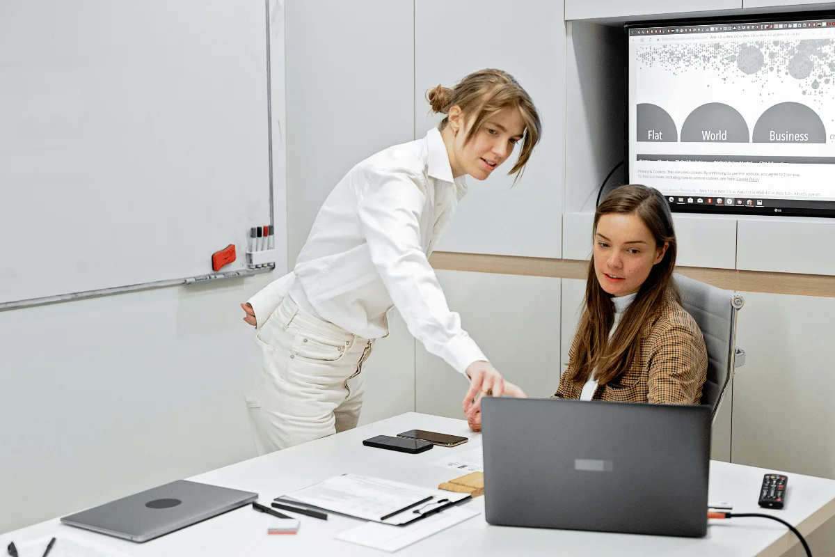 Two women collaborating on laptop in office meeting.