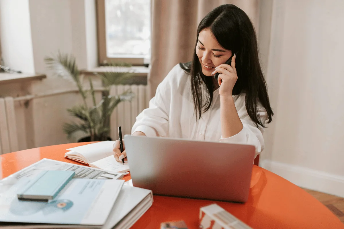 Smiling businesswoman talking on the phone while taking notes at a modern workspace.