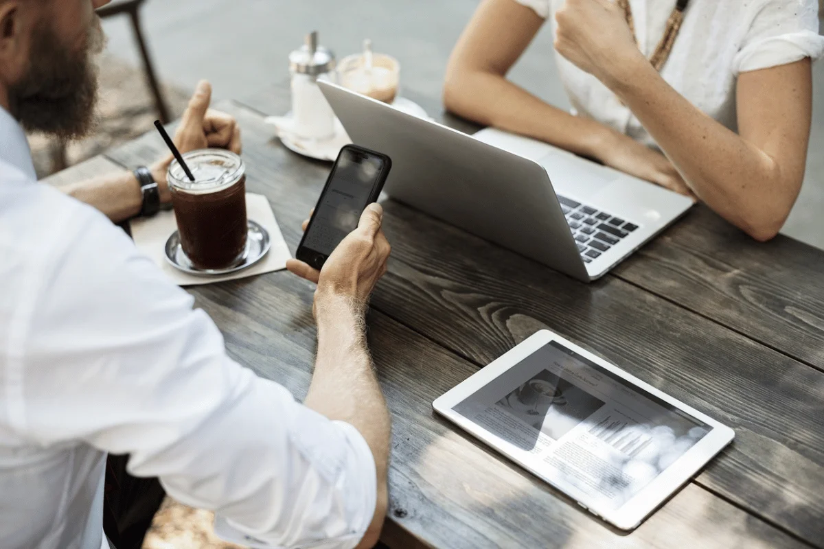 Two professionals working on a laptop and smartphone at an outdoor café.