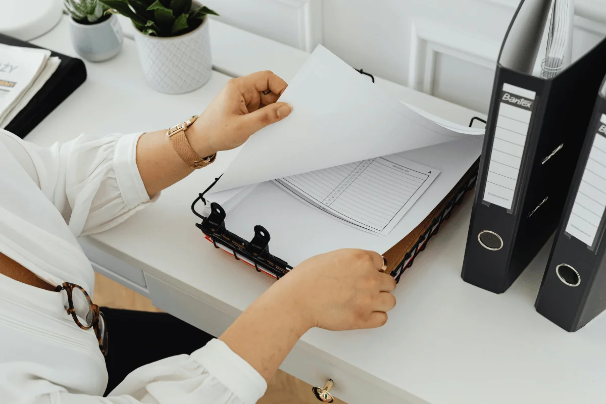 Person organizing paperwork in a binder at a clean office desk.