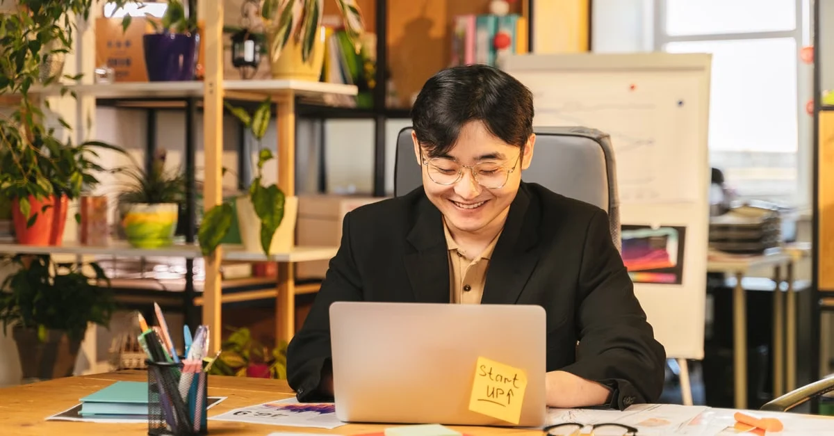 Business professional working at wooden desk with laptop, plants, and office supplies in modern workplace setup.