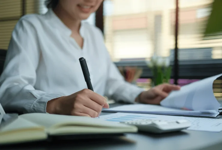 Professional woman analyzing reports and taking notes with a pen in a well-lit office space.