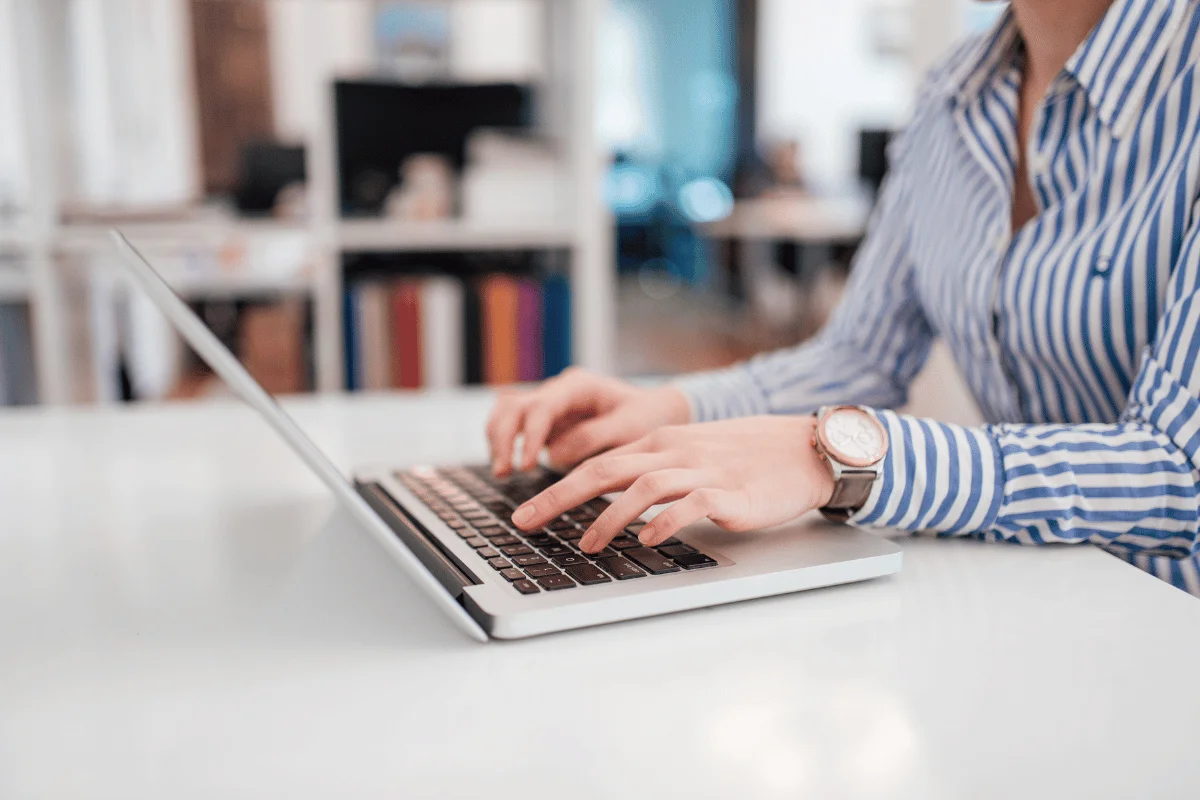 Professional woman in a striped shirt typing on a laptop at a modern office desk.