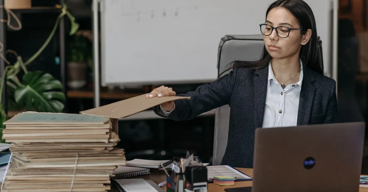 Professional woman at desk reaching toward stacked documents while working, demonstrating fractional executive assistant.