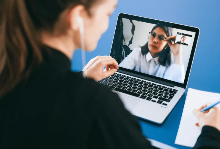 A person on a video call using a laptop, with handwritten notes and a blue background, engaged in a virtual conversation.