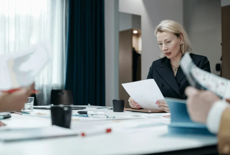 A group of professionals engages in a meeting, reviewing documents and discussing ideas around a conference table with notebooks and pens.