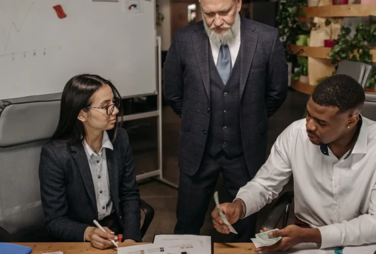 Executive assistant vs virtual assistant comparison during office meeting with three professionals reviewing documents.