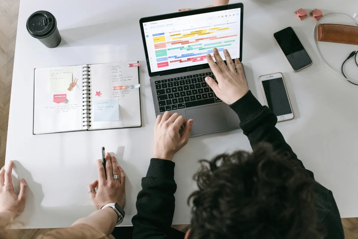 A group of people working collaboratively on a project with a laptop and planner on the desk.