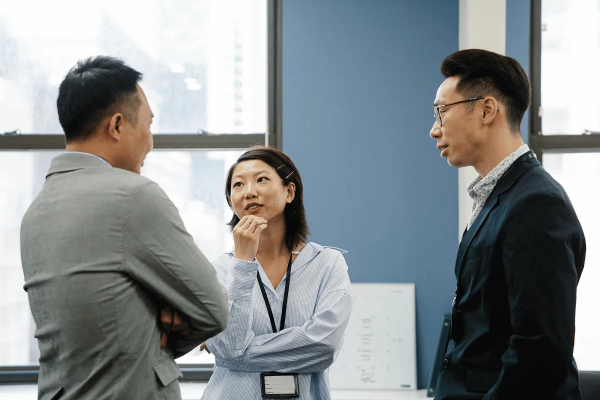 Team members having a thoughtful conversation in a corporate office with large windows.