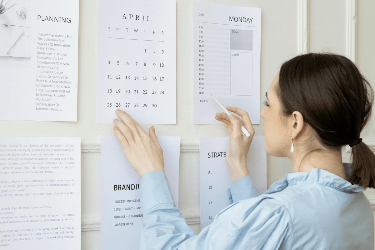 Woman organizing strategy and planning documents on a wall with a pen and calendar.