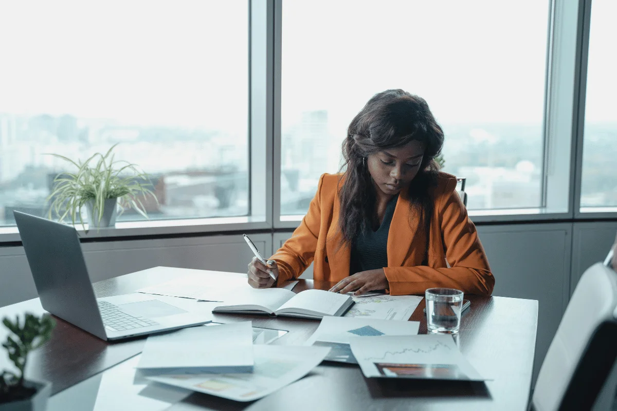 A businesswoman analyzing documents and taking notes at a corporate boardroom table.
