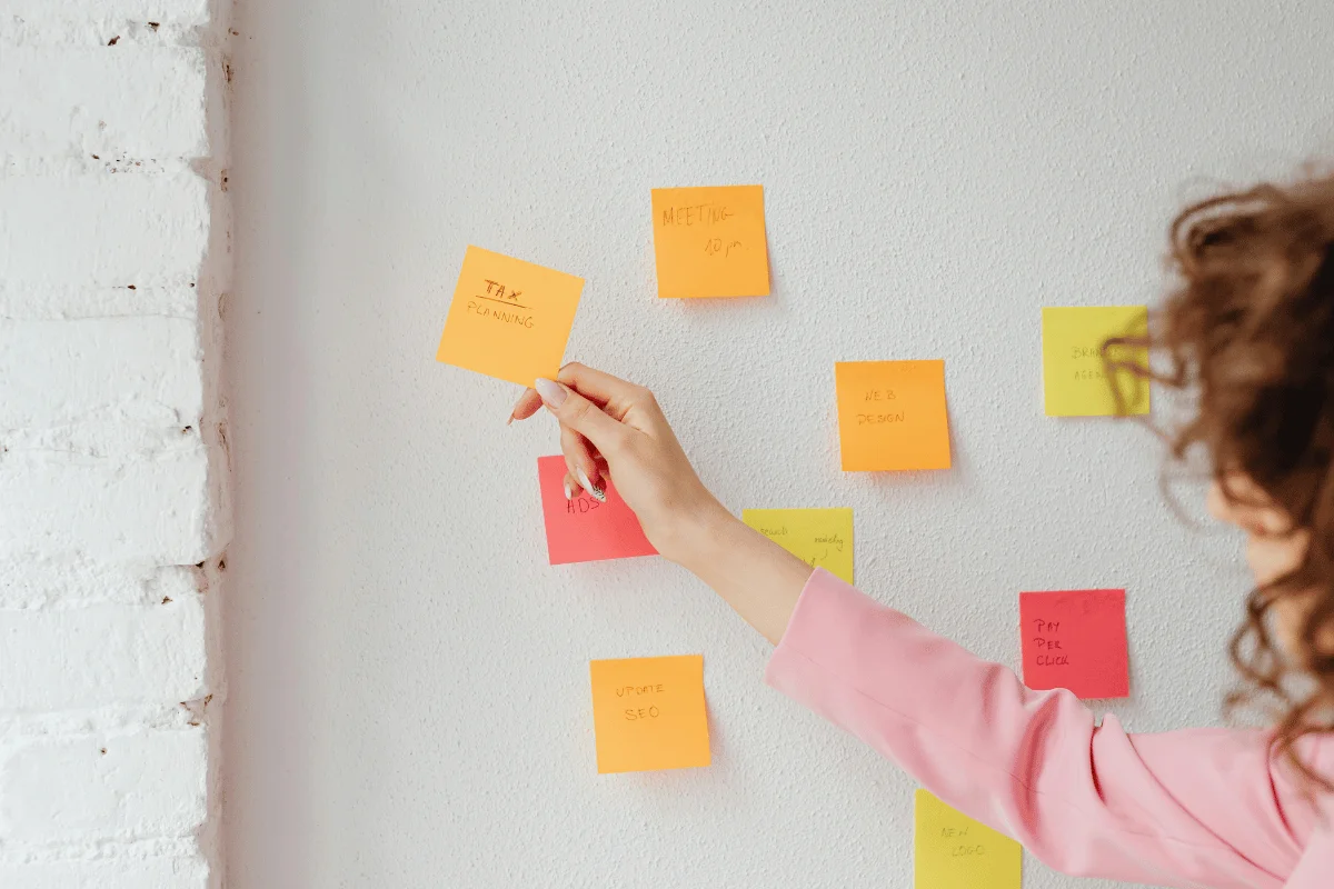 Woman organizing colorful sticky notes on a white wall for task planning.