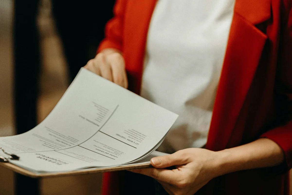 A woman holds a clipboard with documents while reviewing the papers in her hands.