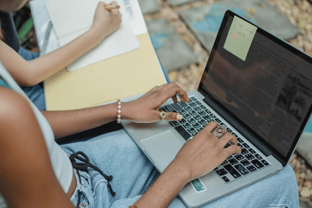 Person typing on a laptop with a sticky note reading "today is a happy day" on the screen.