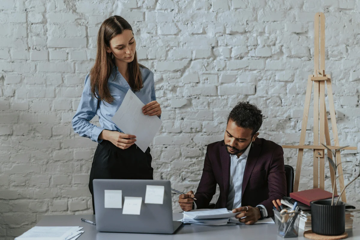 Two colleagues reviewing documents at a modern office desk.