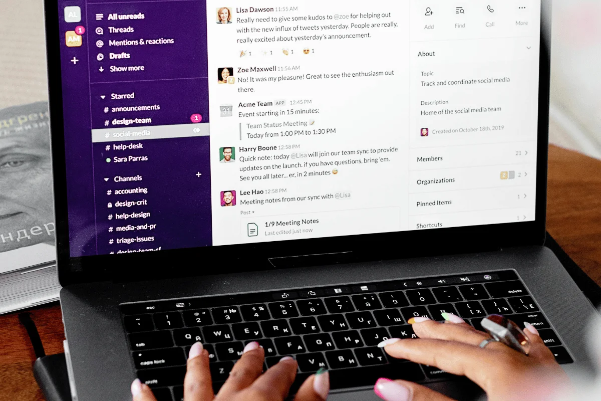 Hands typing on a laptop displaying a Slack workspace with team communication and project updates.