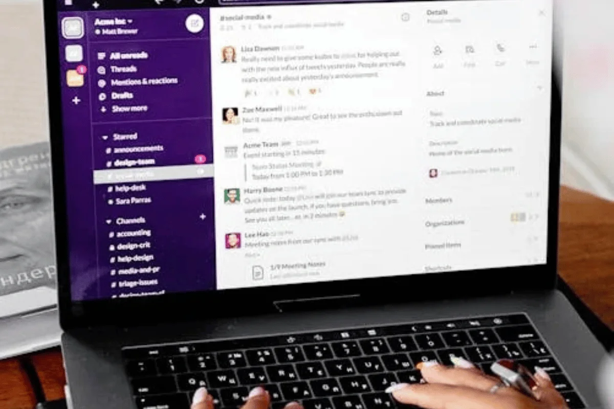 A person types on a laptop displaying a messaging app, showing team discussions and project details in a vibrant interface.