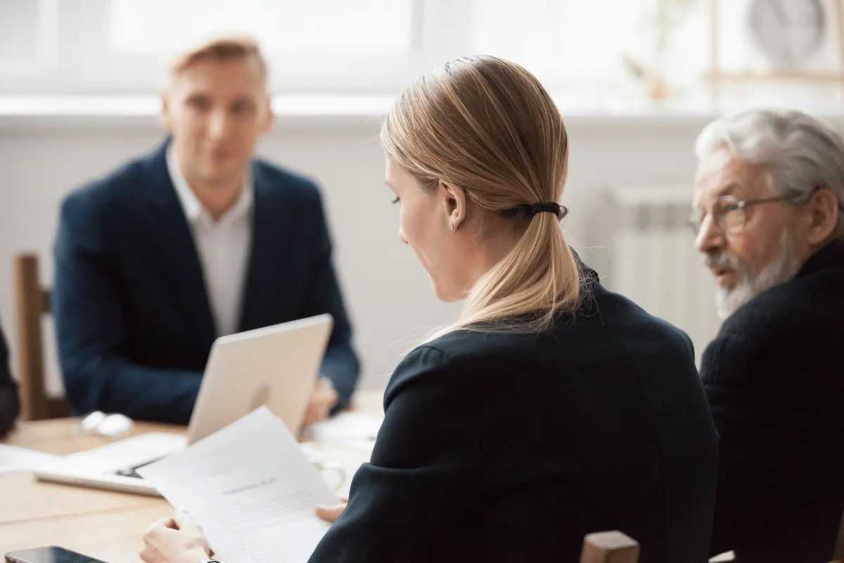 A group of professionals engaged in a meeting, with one person reviewing documents while others observe attentively.