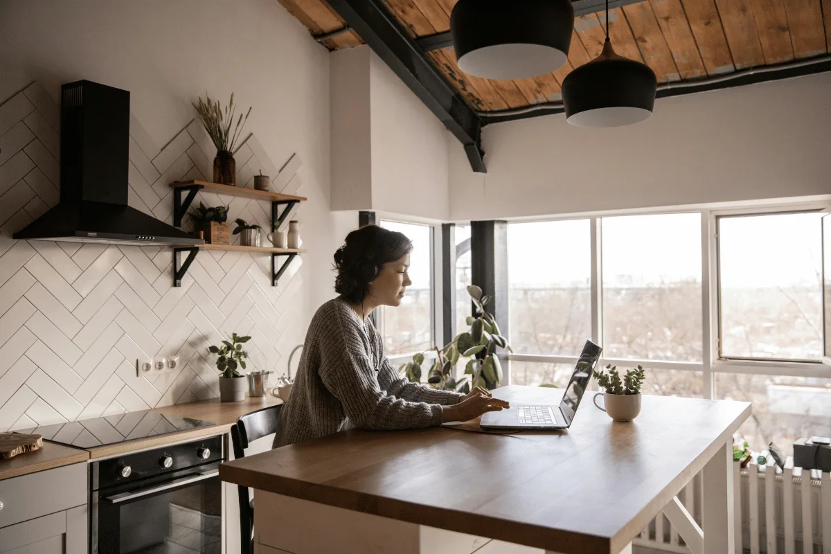 Freelancer typing on a laptop at a wooden kitchen island with a cozy interior.