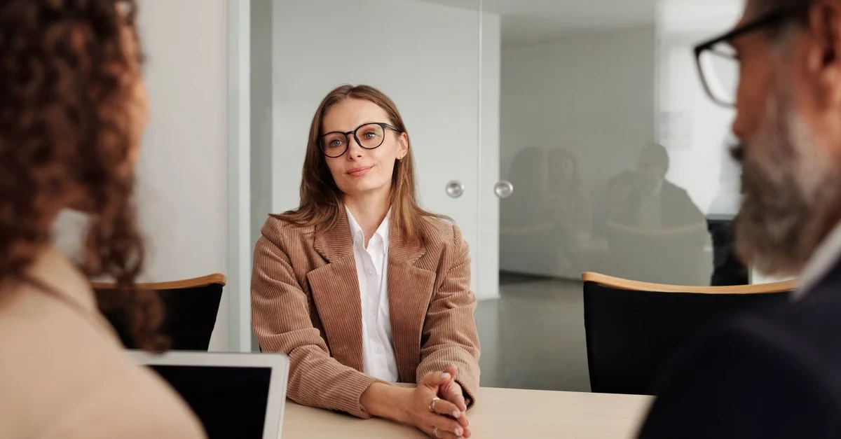 Professional woman in glasses conducting executive assistant interview questions with candidates at office table.