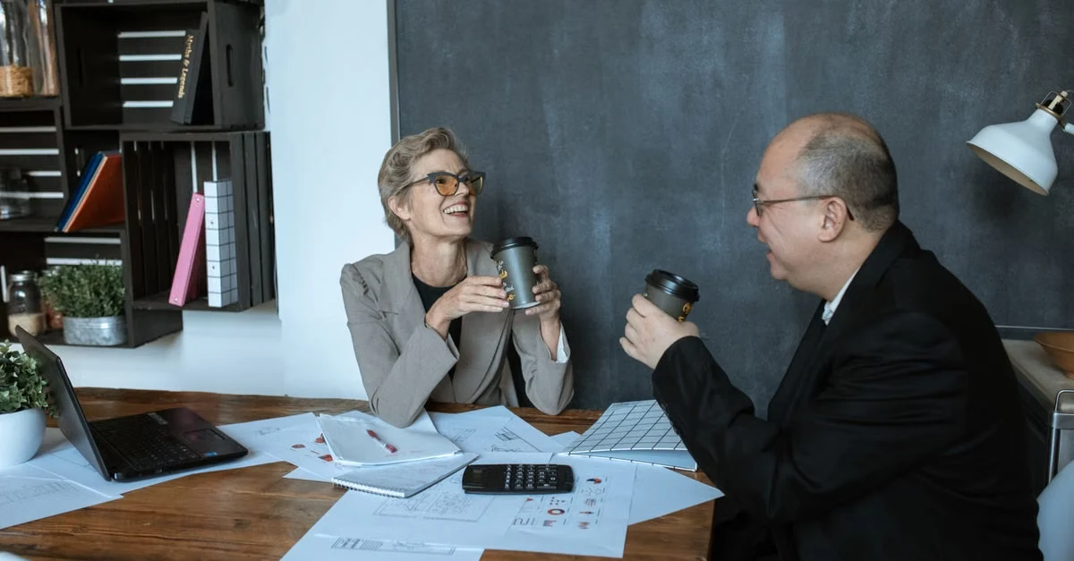 Two professionals discussing executive assistant interview questions at a wooden desk with documents and laptop.