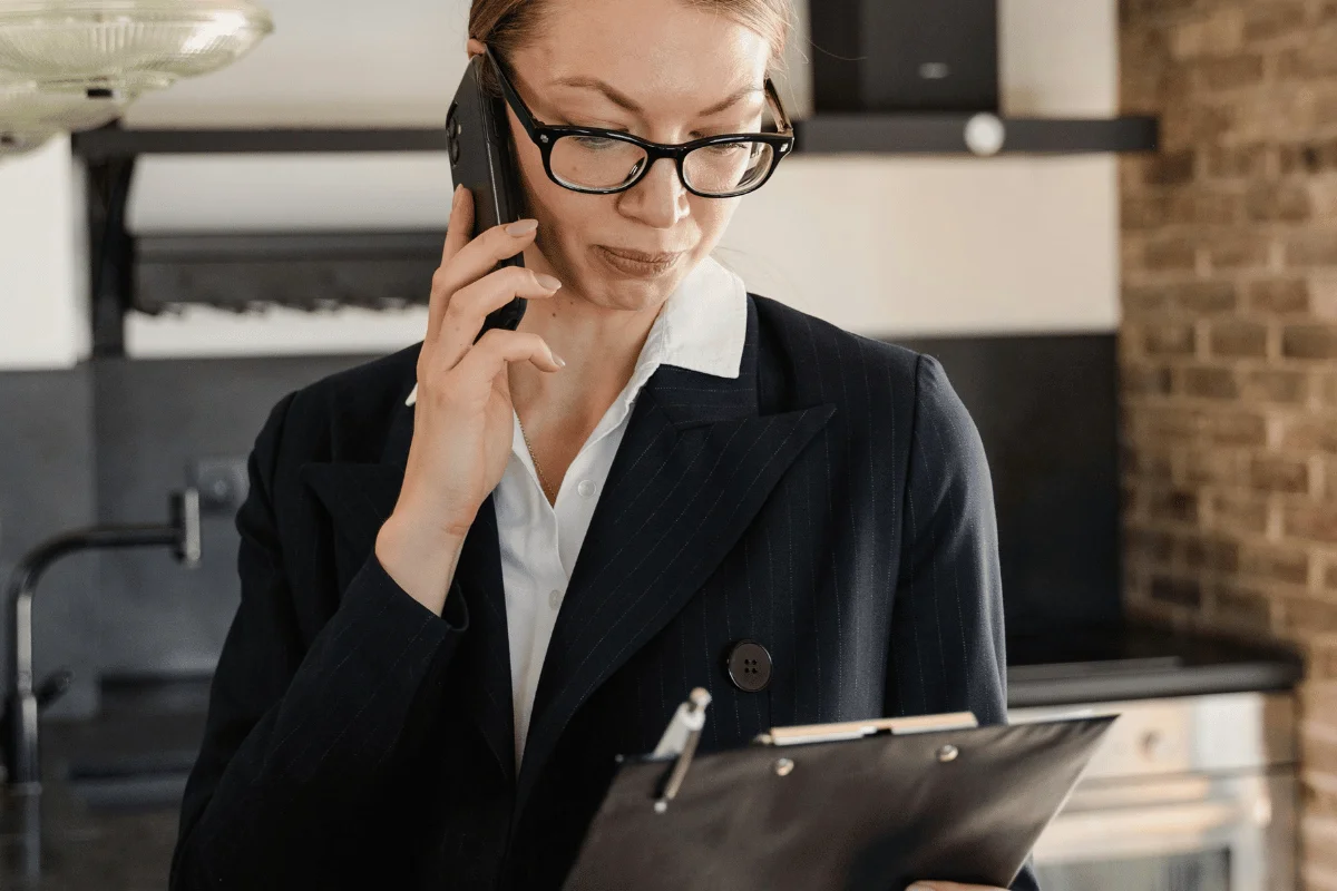 Professional woman speaking on phone while reviewing clipboard notes.