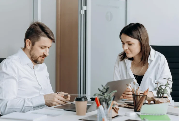 Two coworkers discussing documents at a modern office desk.