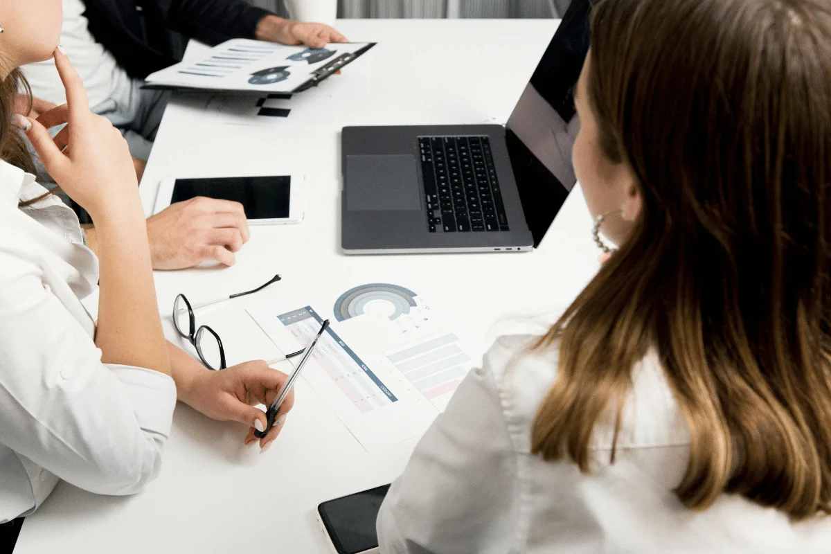 Close-up of a group meeting with data charts, a laptop, and discussion on business strategy.
