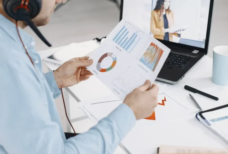 Man reviewing analytics charts during virtual meeting with female professional on laptop screen.