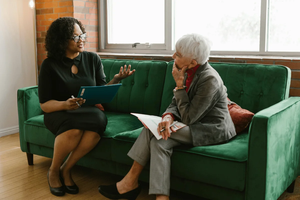 Two women seated on a green couch, engaged in conversation.