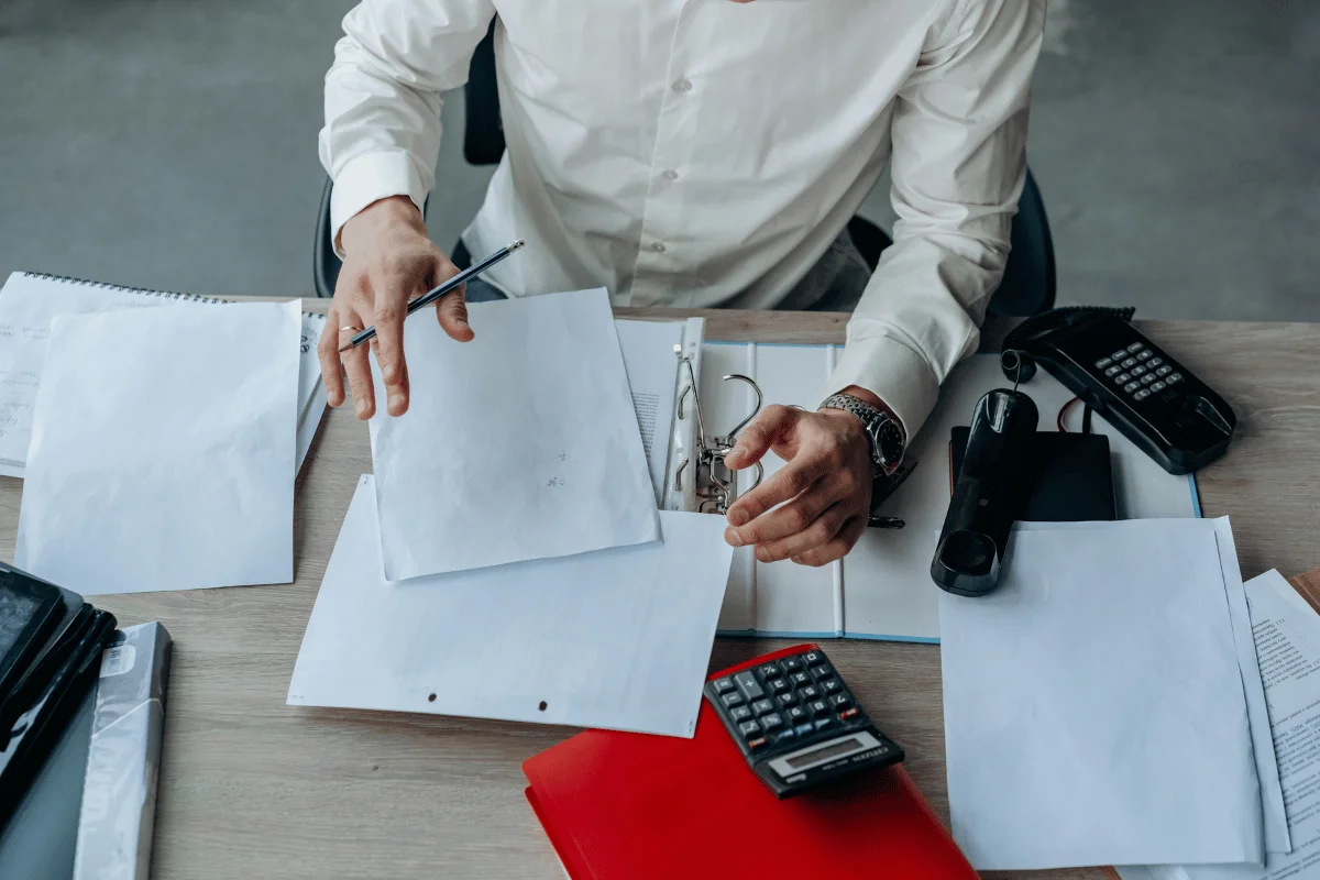 Businessman organizing documents at desk with calculator.