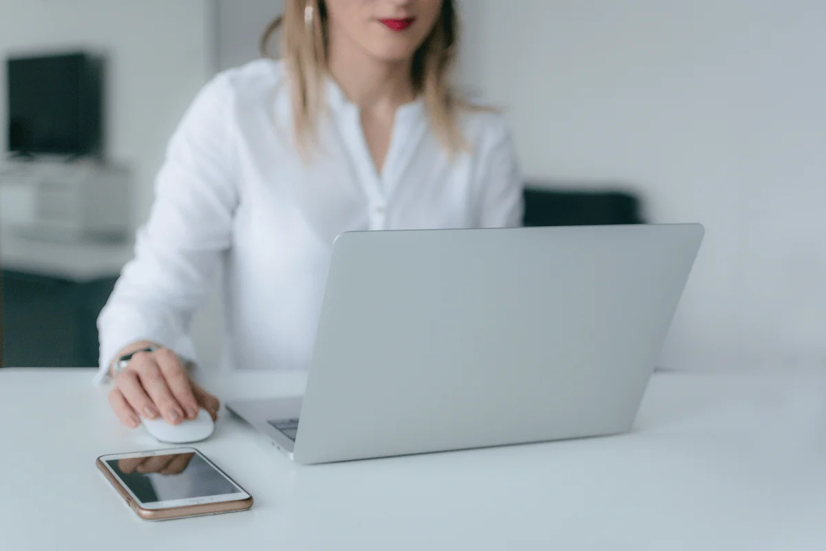 Virtual assistant working on laptop with smartphone on desk.