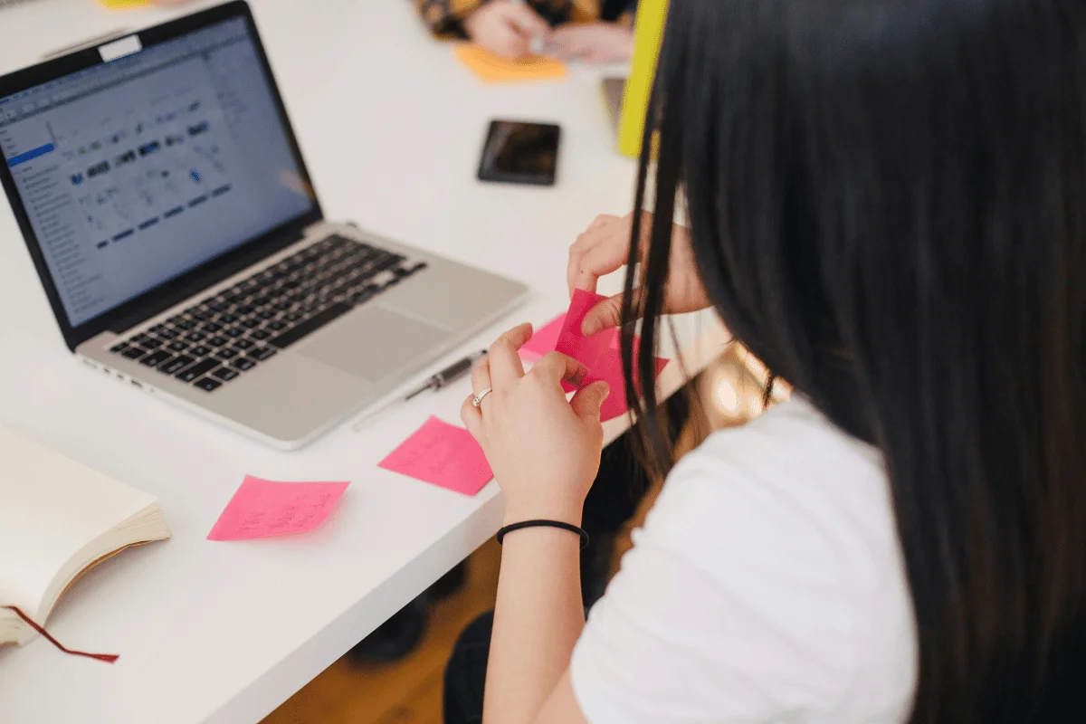 Woman planning tasks with sticky notes while working on a MacBook at a coworking space.
