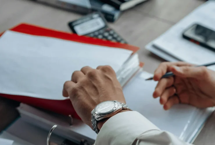Close-up of hands working on documents with a pen and binder.