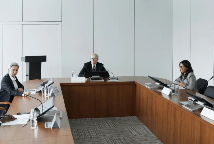 A group of professionals are sitting around a U-shaped conference table in a modern meeting room.