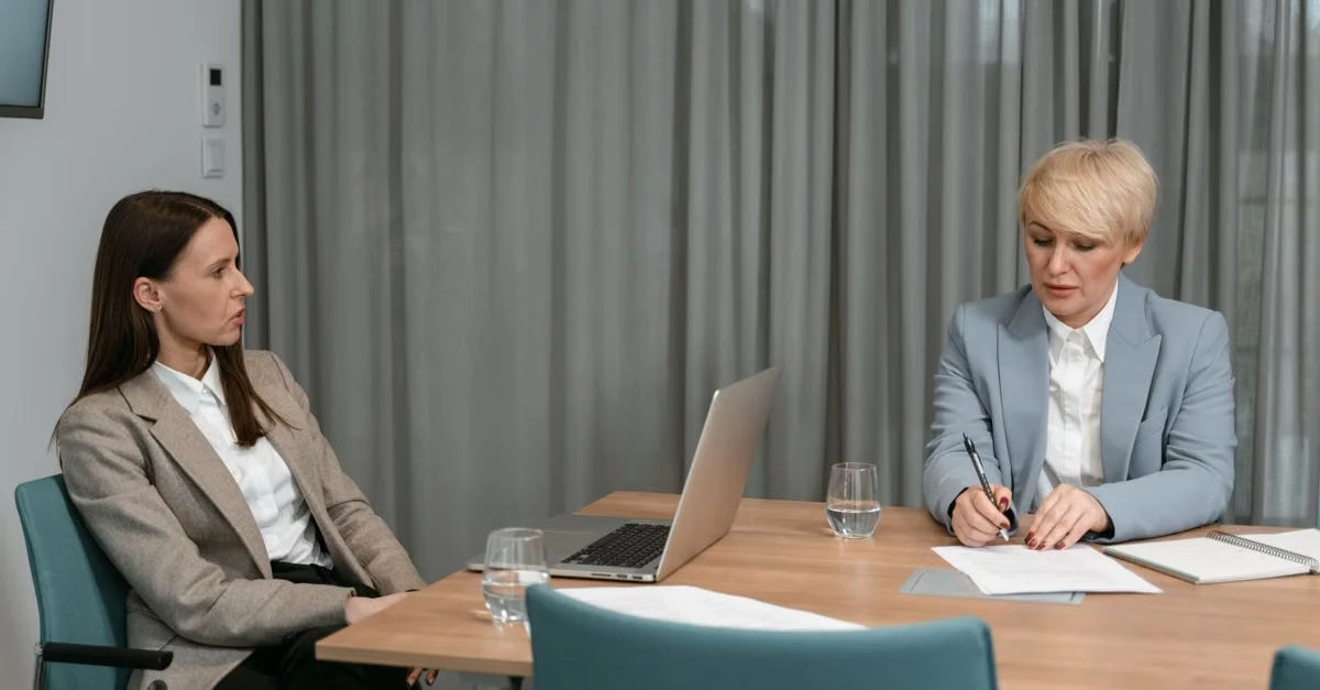 Two professional women conducting a job interview at wooden table, discussing executive assistant skills and qualifications.