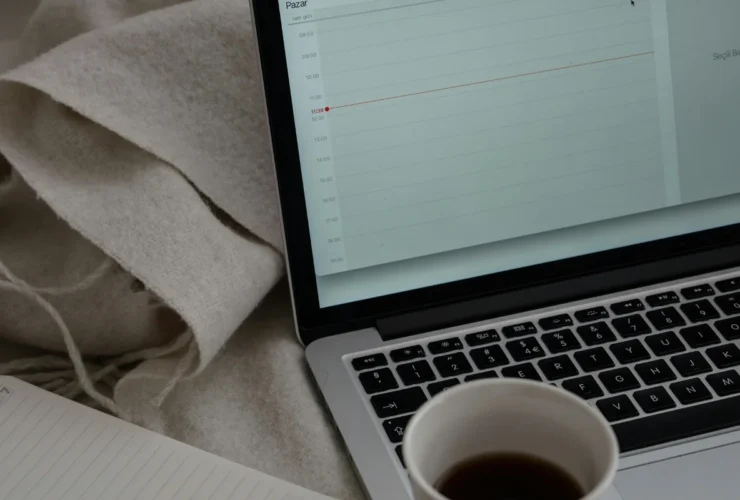A laptop displaying a calendar next to a cup of coffee and a soft gray blanket.