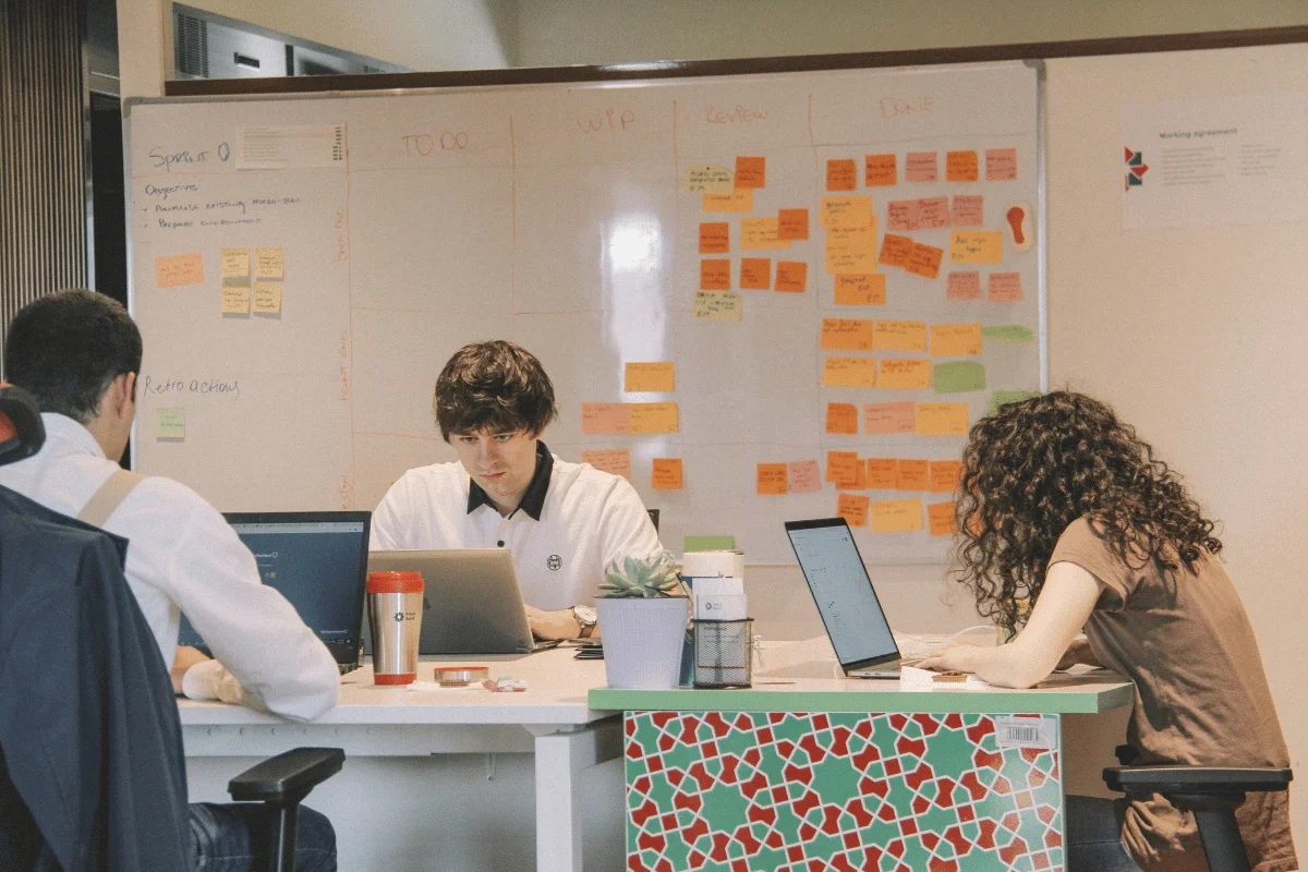 Team collaborating at a desk with a Kanban board covered in sticky notes.