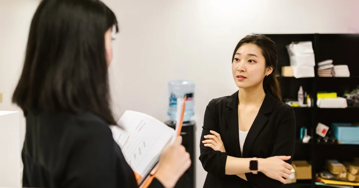 Two professionals discussing in office, demonstrating key executive assistant skills during business conversation.