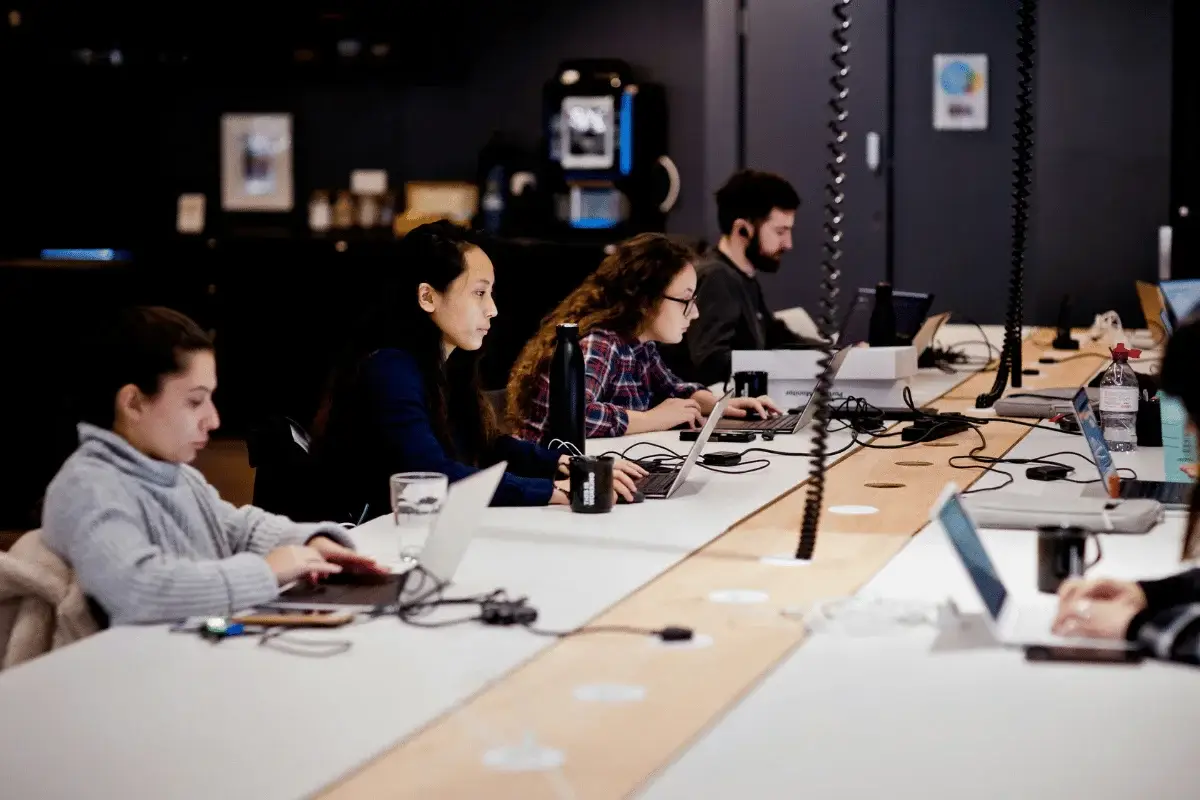 A focused team working on laptops in an open office space with cables and water bottles on the table.