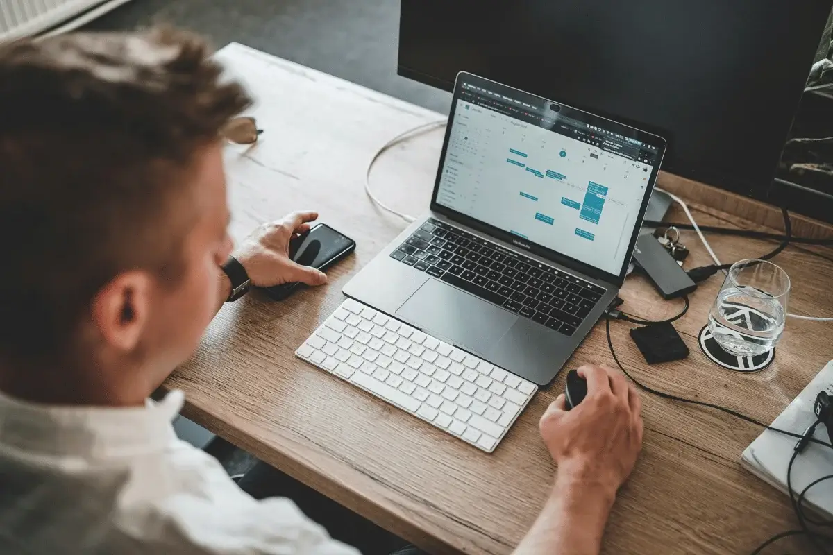 Man using a laptop and phone simultaneously at a tidy office desk.