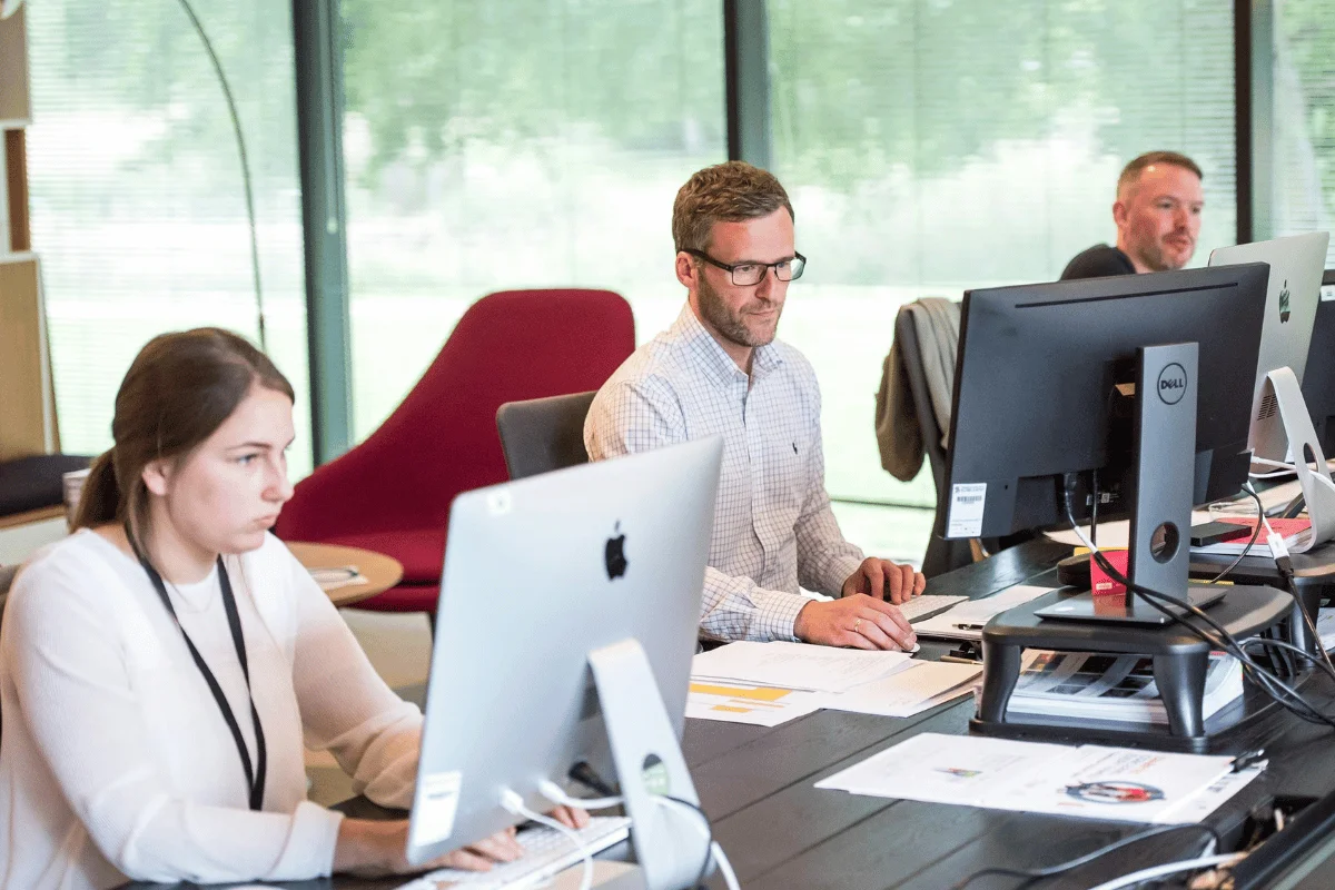Executive assistants working at office desks with desktop computers.